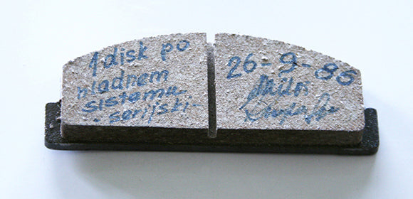 A split brake pad sample with handwritten notes and a date