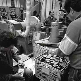 Black-and-white photo of factory workers with crates of pressed parts