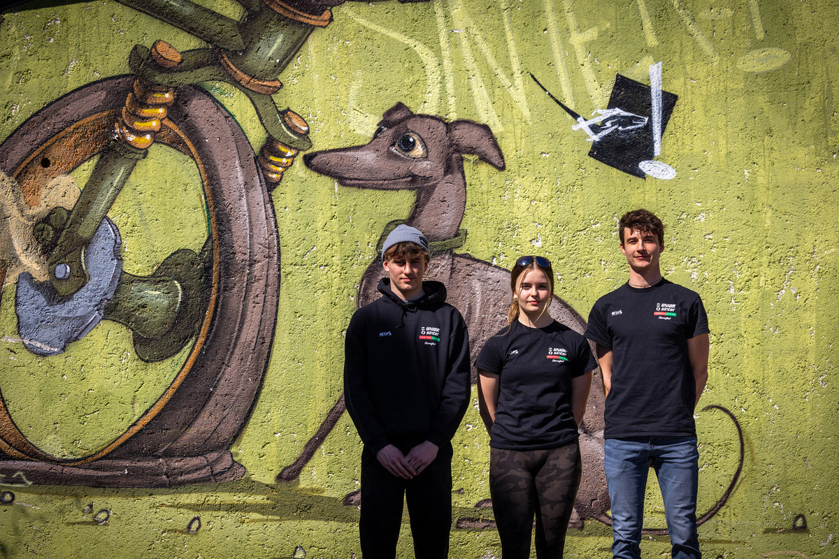 Three Unior Sinter Factory Racing team members in front of a painted mural