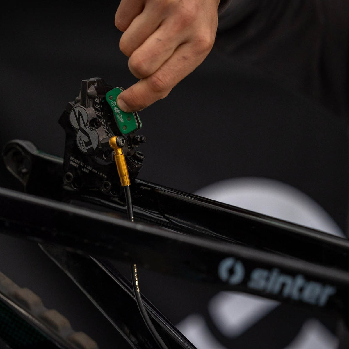 A mechanic fits a green Sinter brake pad into a mountain bike's disc brake caliper