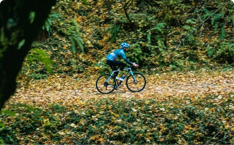 Mountain biker riding through autumn forest trail with fallen leaves