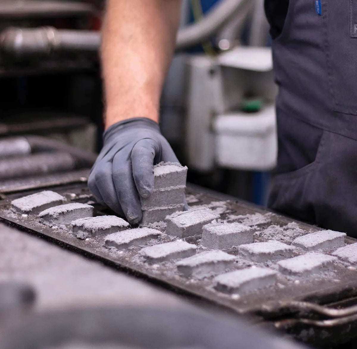 A gloved hand lifts moulded friction-material blocks from a production tray