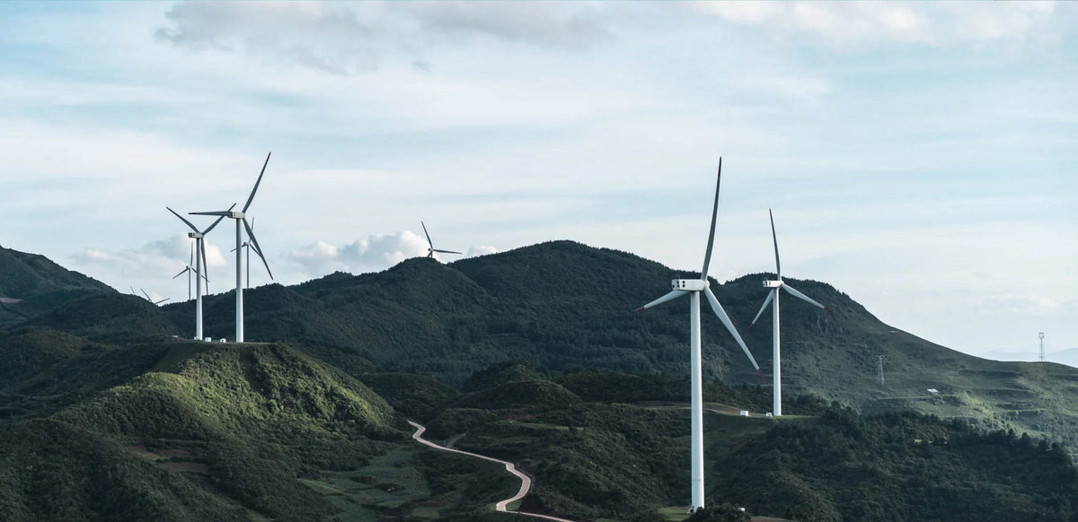 Vetrne turbine na zelenih gorskih pobočjih pod oblačnim nebom, ki predstavljajo trajnostne industrijske uporabe